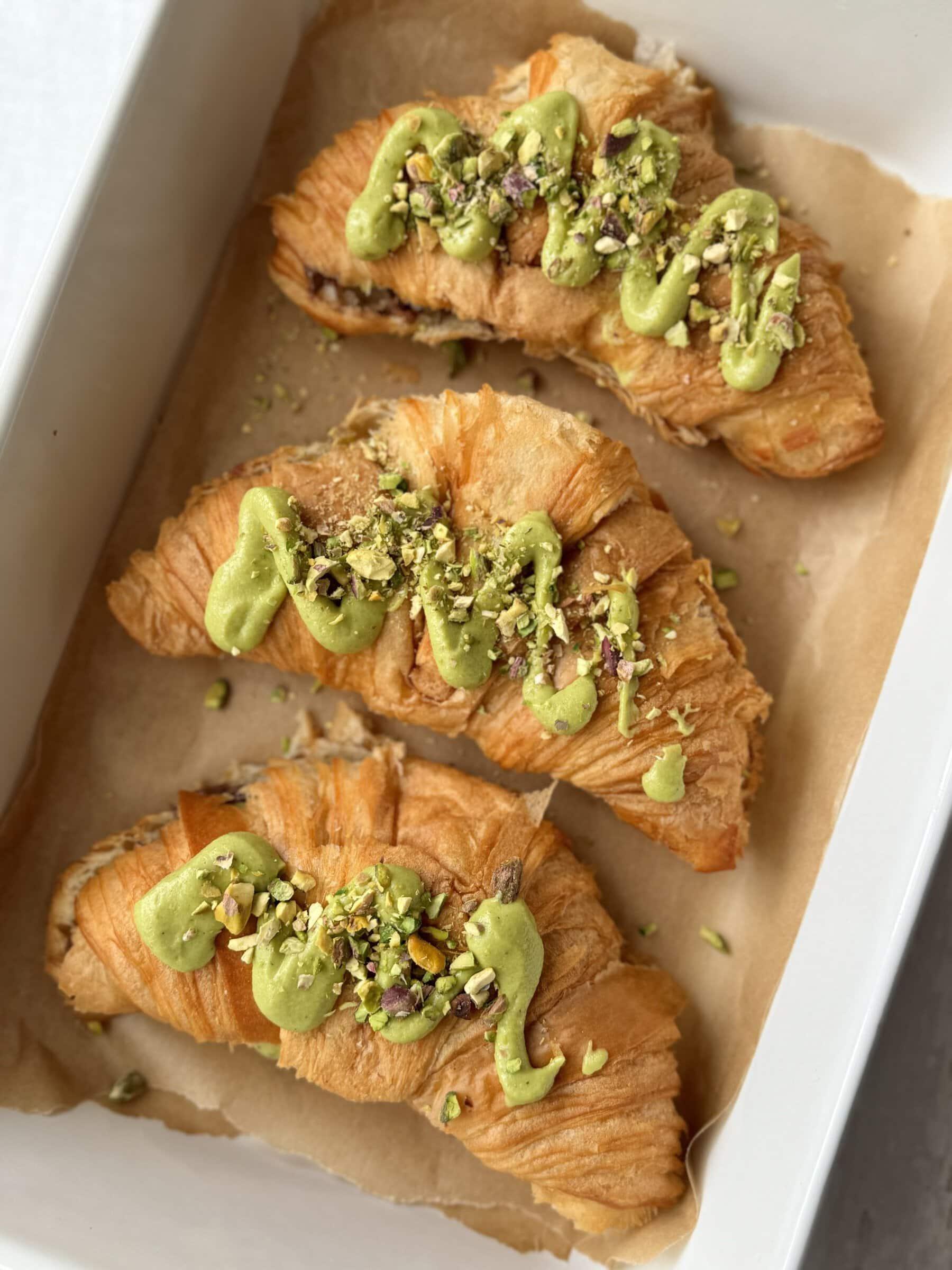 A spiral pistachio croissant dusted with crushed pistachios on a white plate