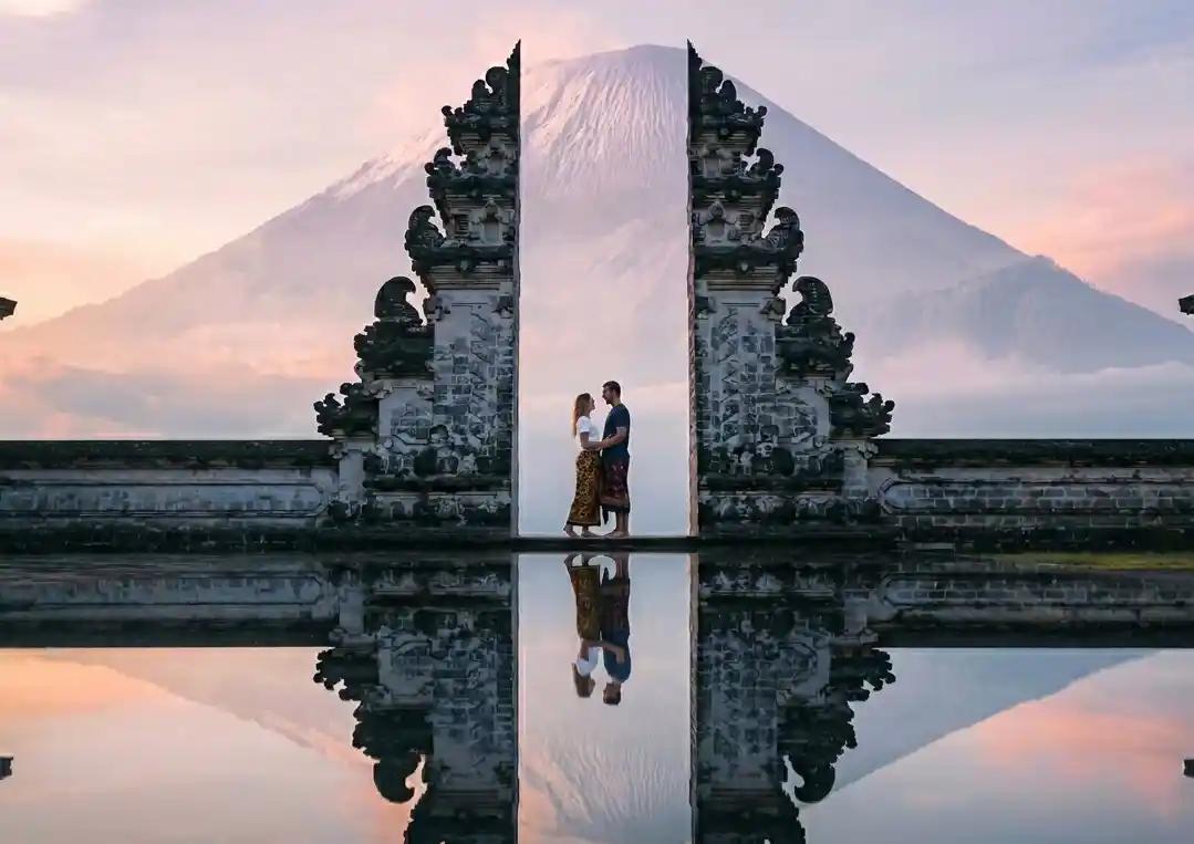 Ornate Balinese stone gate pillar with intricate carvings, Mount Agung volcano rising behind lush green jungle, Bali