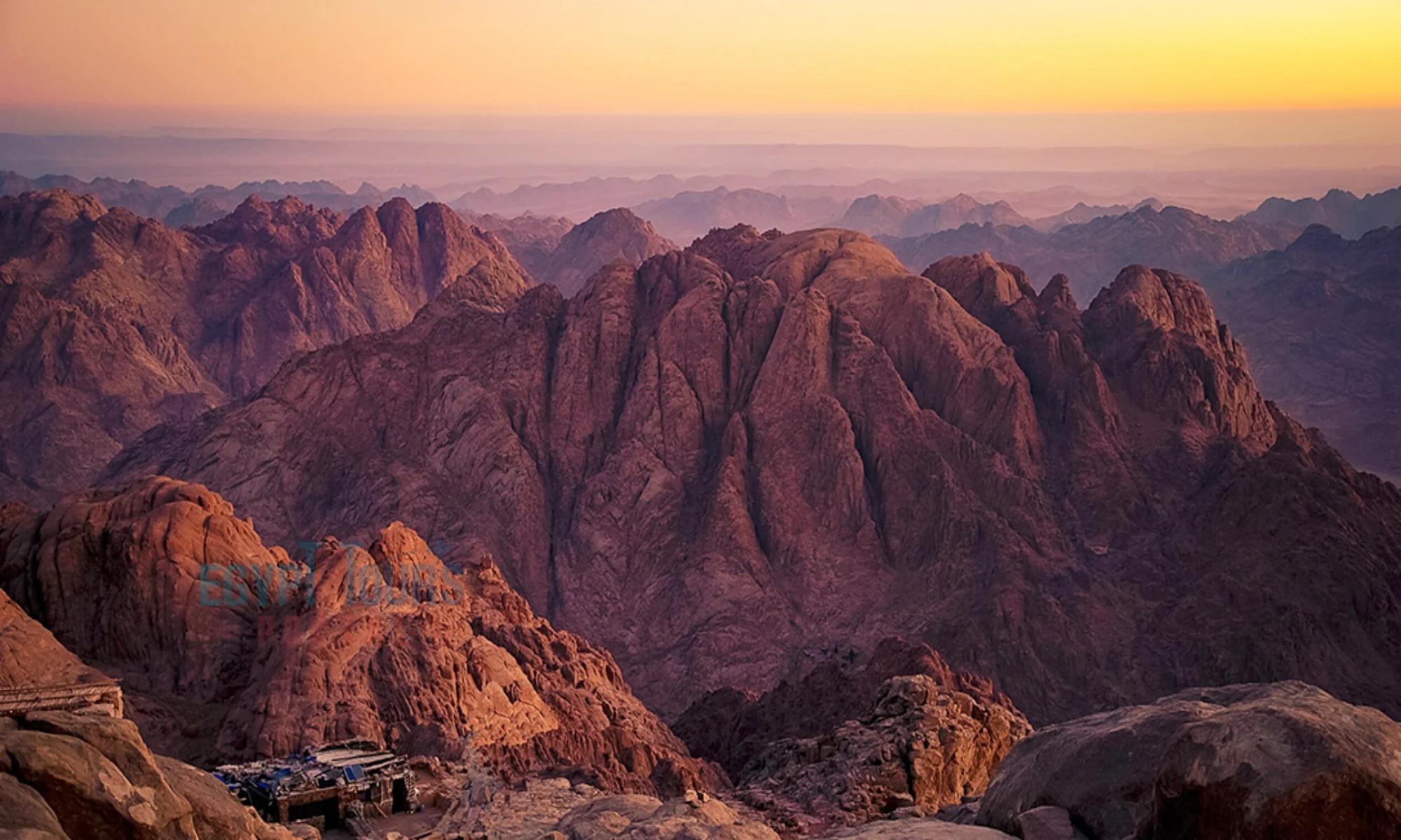 Hikers approaching the summit of Mount Sinai at dawn with granite peaks in the background