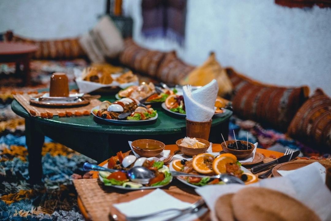Traditional Lebanese mezze spread with small plates, orange slices, and clay bowls on low floor tables with woven cushions