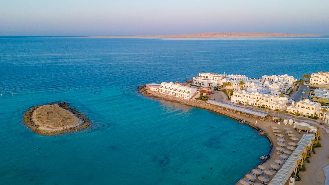 Aerial view of white domed resort buildings along a curved Red Sea coastline in Hurghada, with turquoise water and a small rocky islet