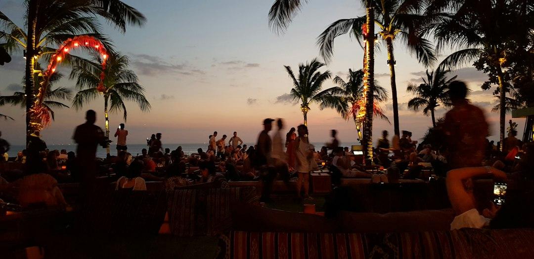 Crowded beachfront bar at sunset in Seminyak Bali with palm trees, string lights, and silhouetted guests