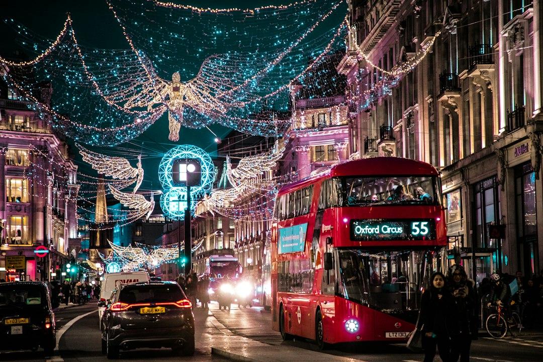 Red double-decker bus route 55 to Oxford Circus beneath glowing angel Christmas lights on Regent Street at night