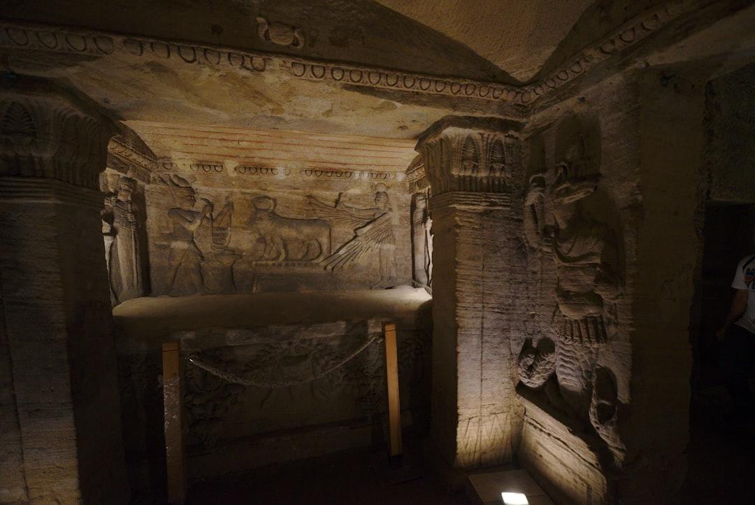 Dimly lit underground chamber in Kom El Shoqafa with carved Egyptian relief scenes and decorated stone columns