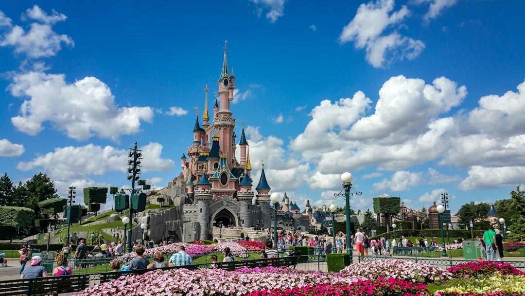 Sleeping Beauty Castle at Disneyland Paris surrounded by pink flower beds and visitors on a sunny day