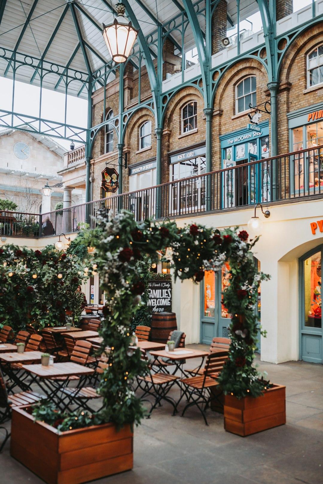 Floral arch with fairy lights at Covent Garden Market Building, surrounded by outdoor café tables and teal ironwork