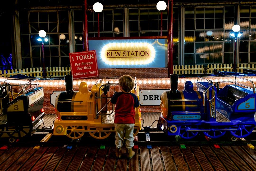 Young child gazing at colorful miniature fairground trains at Kew Station ride, lit up at night during Christmas at Kew