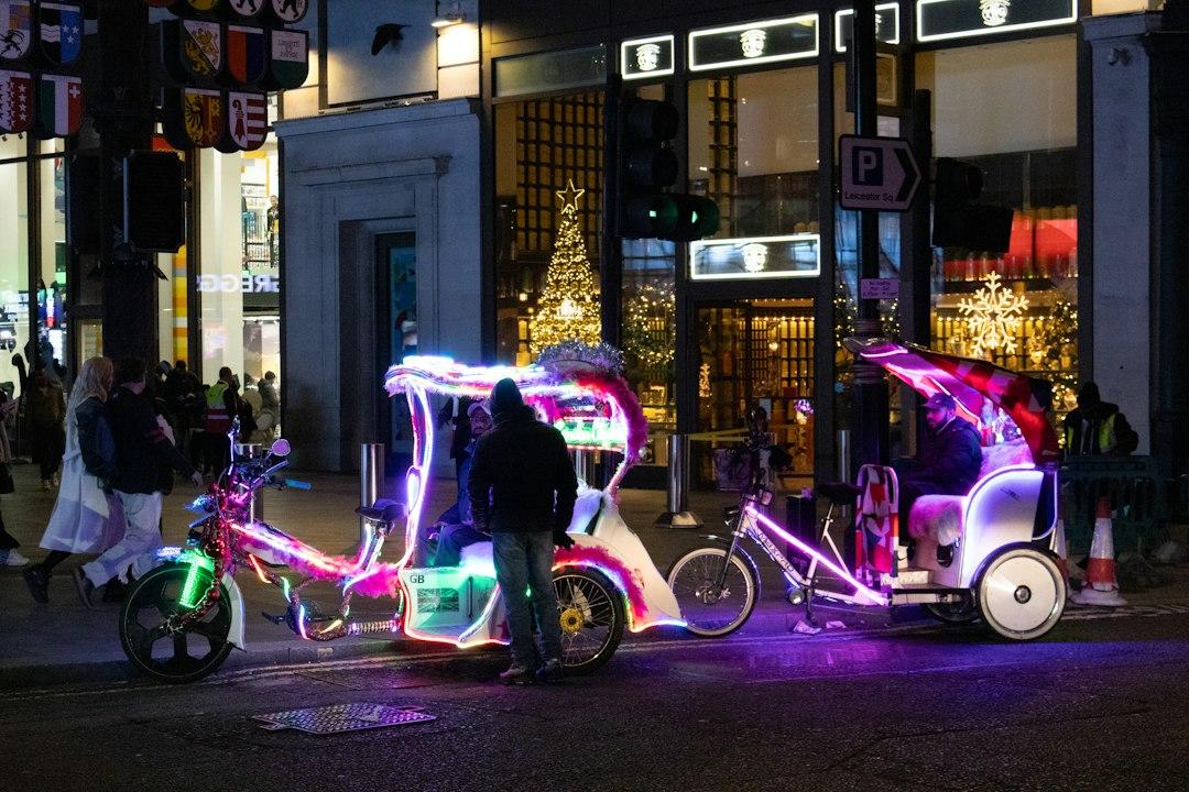 Neon-lit pedicabs parked on a London street at night near Leicester Square with a glowing Christmas tree in the background