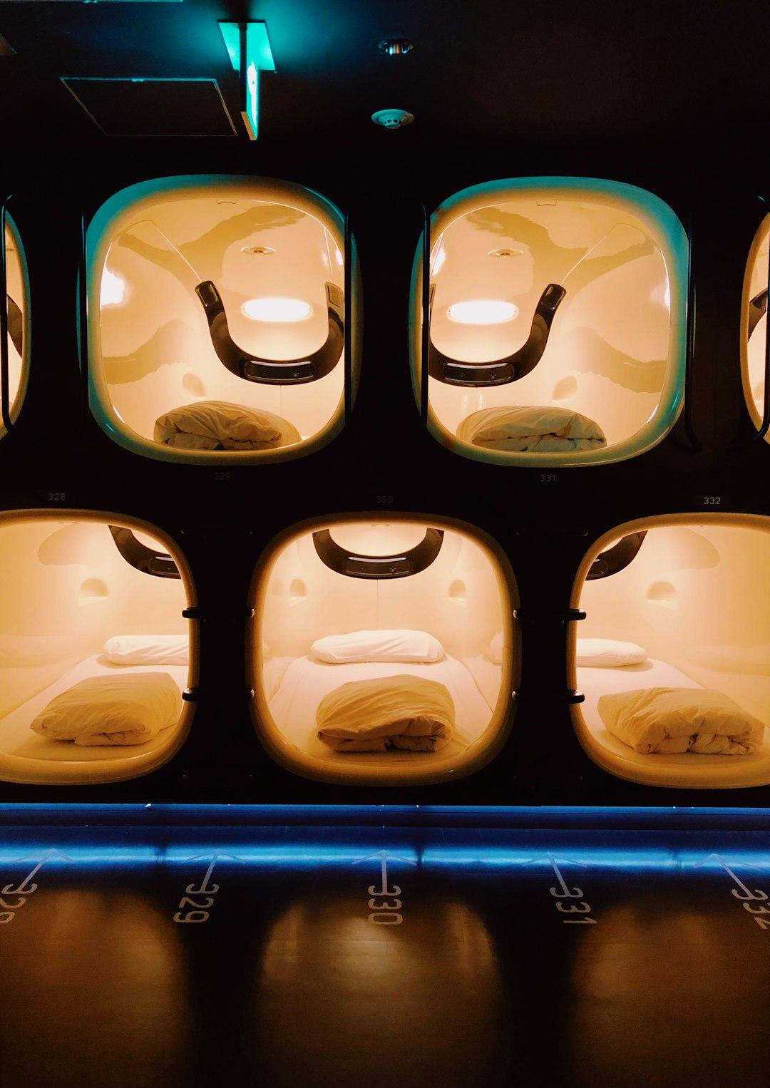 Rows of glowing numbered sleeping capsules with white bedding in a modern Japanese capsule hotel