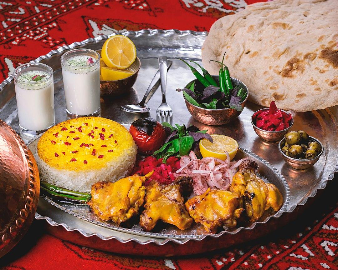 Persian saffron chicken jujeh with turmeric rice, pickled onions, olives, flatbread, and doogh on a silver tray