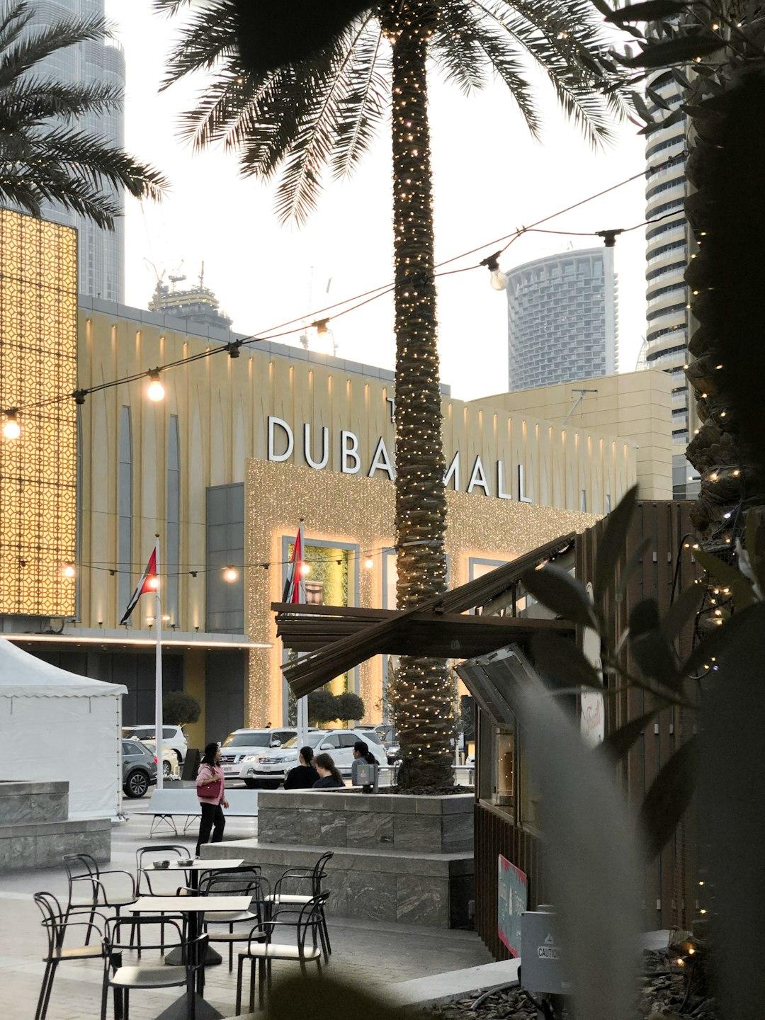 Outdoor café seating with fairy-lit palm trees in front of The Dubai Mall entrance, skyscrapers in background