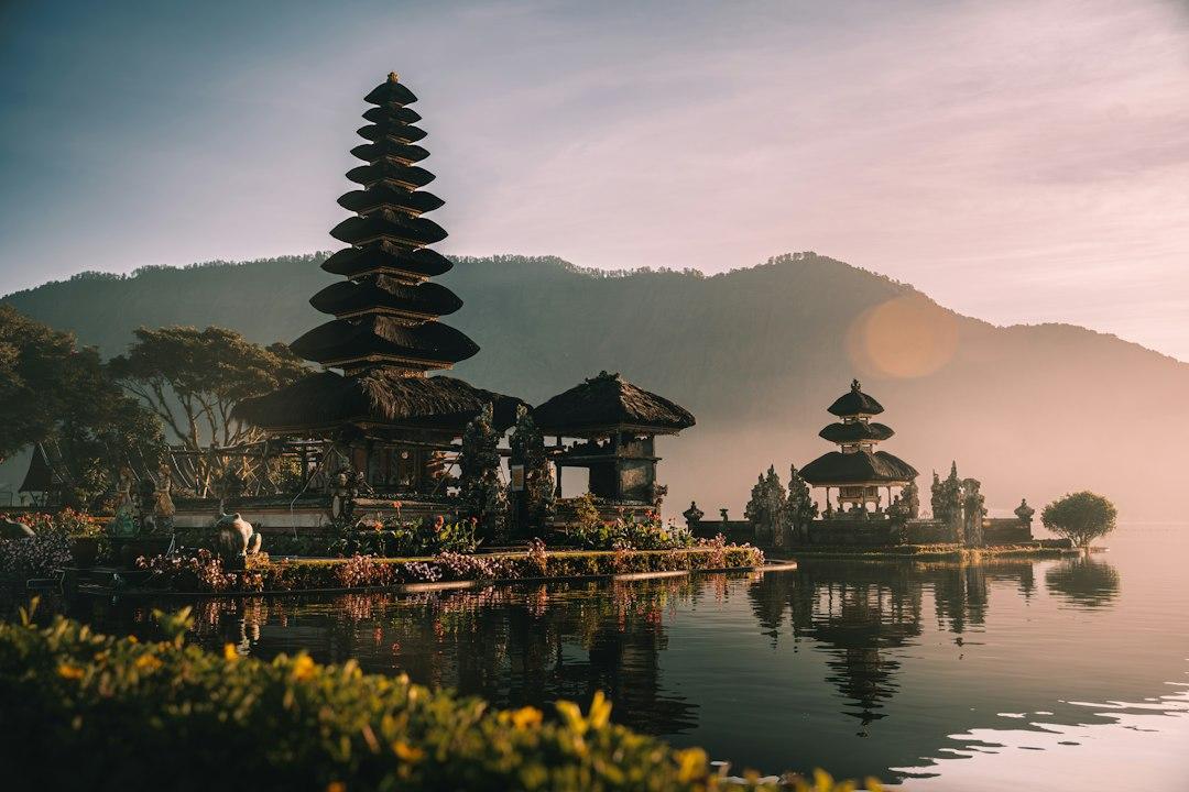 Pura Ulun Danu Bratan temple rising from misty lake waters at sunrise, with layered pagoda and mountain backdrop, Bali