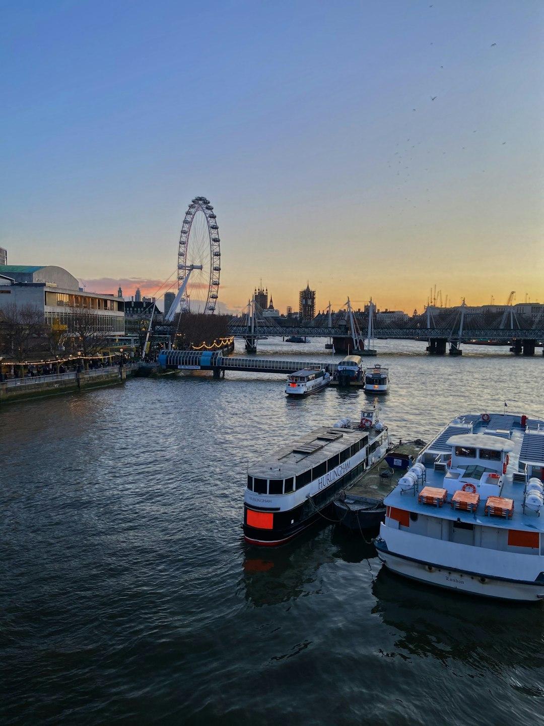 River Thames at sunset with the London Eye, Hungerford Bridge, and moored cruise boats on the South Bank