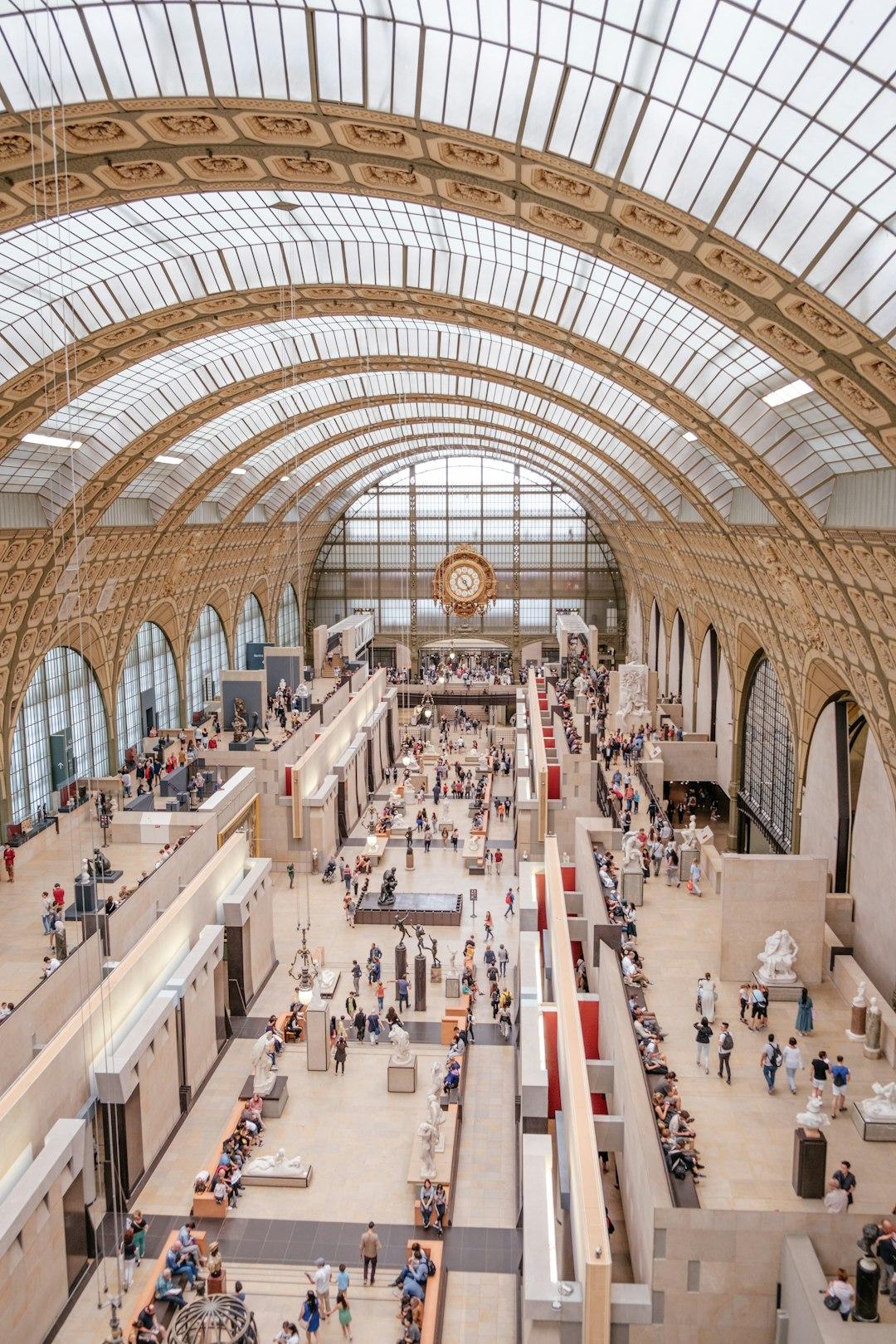 Grand vaulted glass ceiling of Musée d'Orsay's main hall with sculptures and crowds below