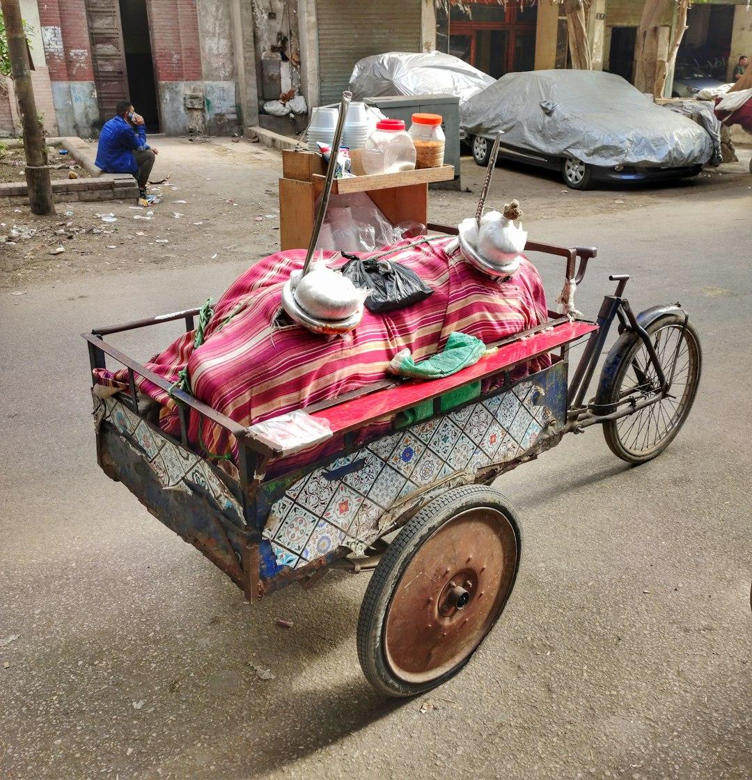 Worn tricycle street food cart with striped cloth, pots, and spice jars parked on a Cairo street