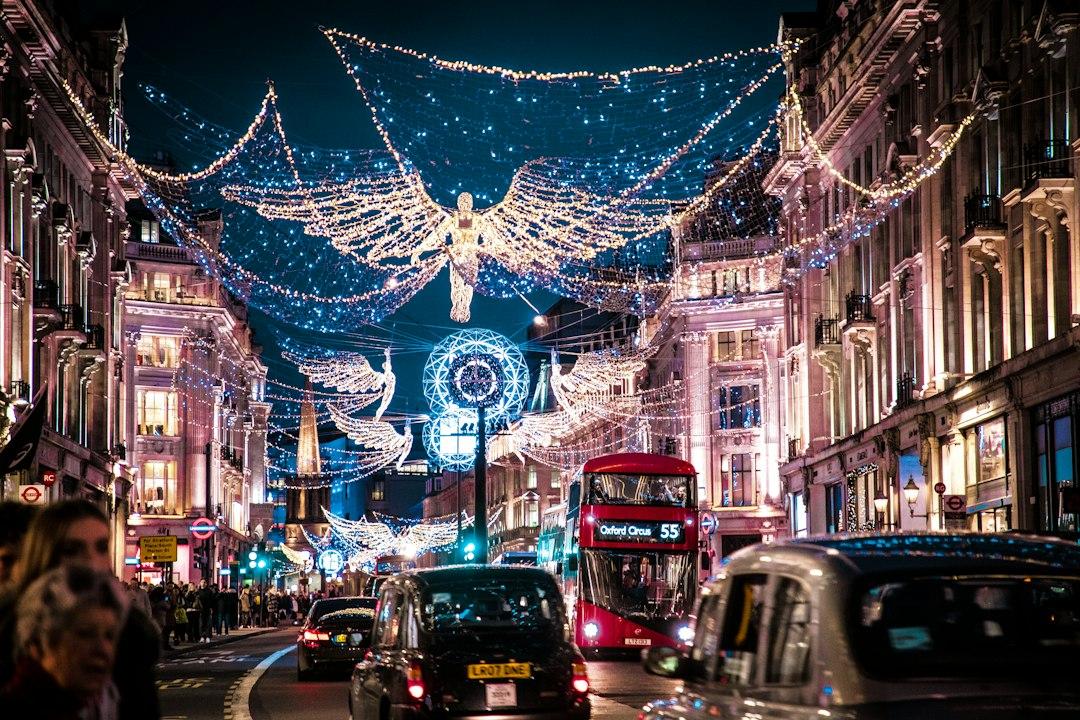 Regent Street London at night with glowing angel Christmas lights above red double-decker bus and black taxis