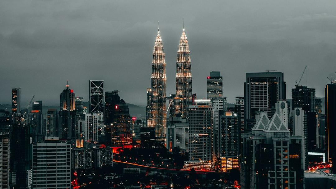 Kuala Lumpur skyline at dusk with illuminated Petronas Twin Towers rising above city buildings under a cloudy sky
