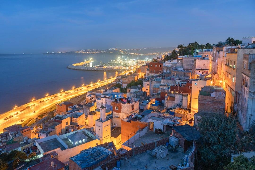Aerial twilight view of Tangier's medina rooftops and glowing coastal boulevard along the strait