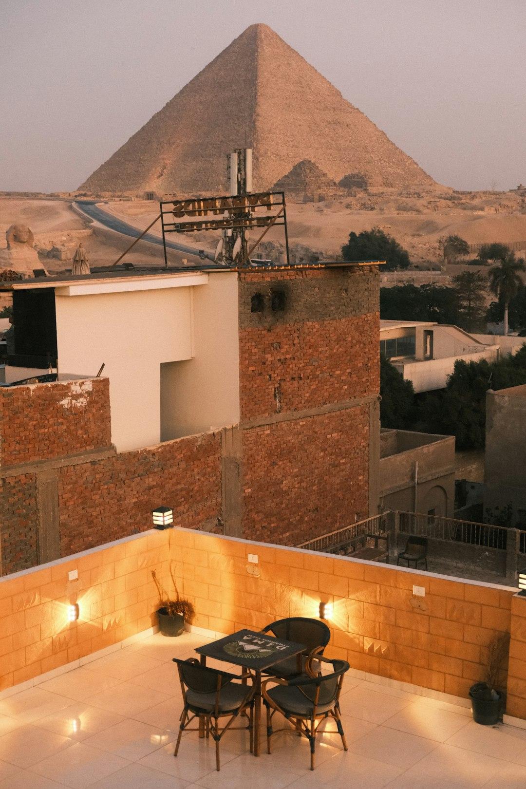 Lit rooftop terrace with table and chairs overlooking Giza cityscape and the Great Pyramid at dusk