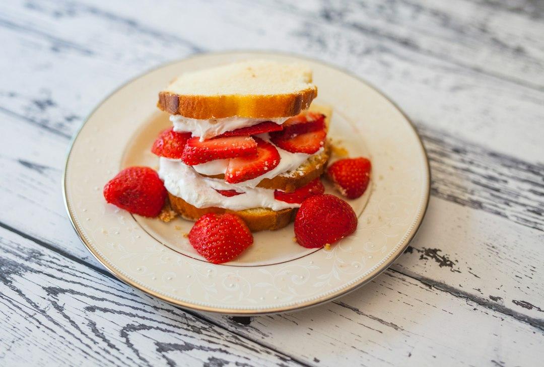 Strawberry shortcake sandwich with whipped cream and sliced strawberries on sponge bread, served on a white plate