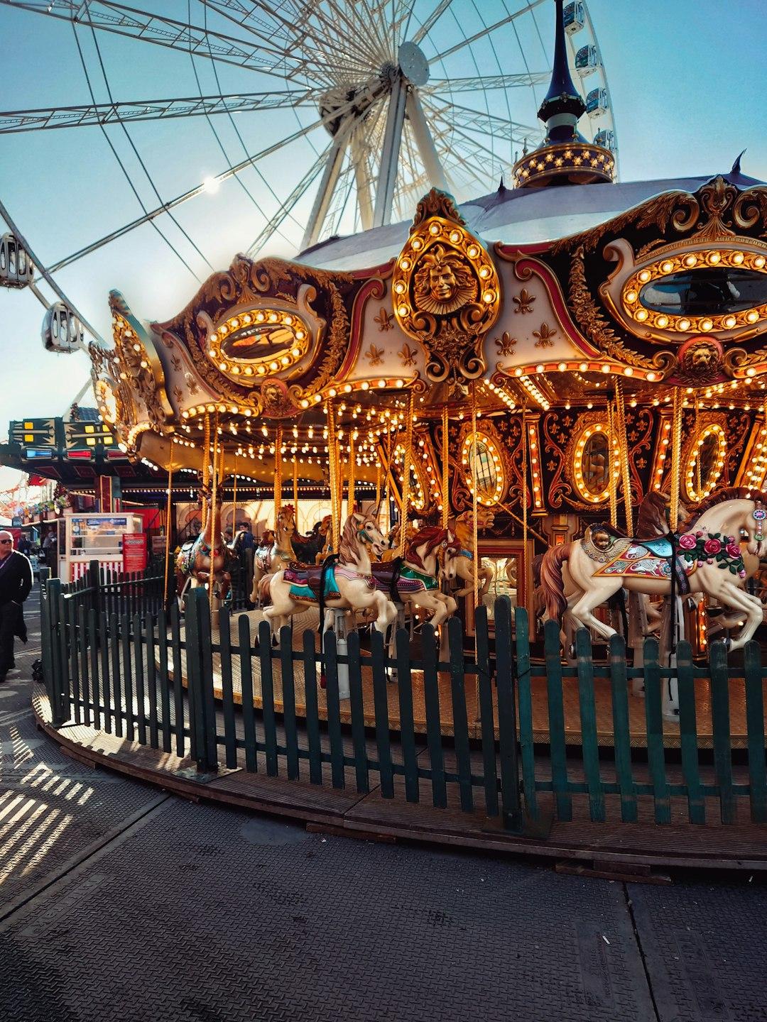 Ornate golden carousel with glowing lights and painted horses at Hyde Park Winter Wonderland, London, with a Ferris wheel behind