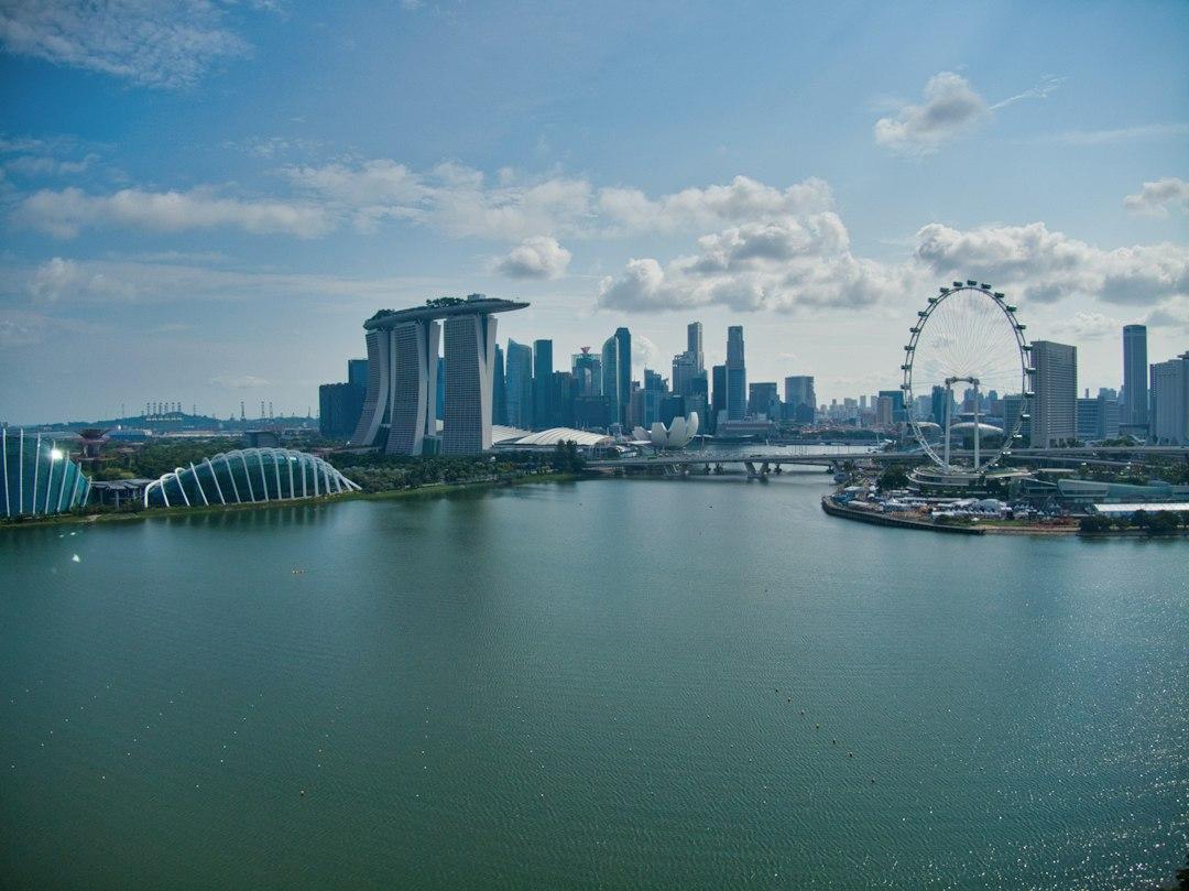 Singapore skyline with Marina Bay Sands, Gardens by the Bay domes, Singapore Flyer, and calm bay waters under blue sky