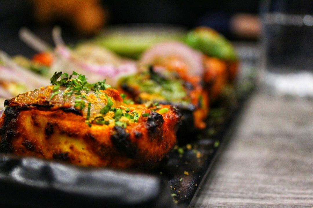 Charred tandoor-grilled paneer skewers topped with fresh coriander and spiced crumbs on a dark sizzler plate