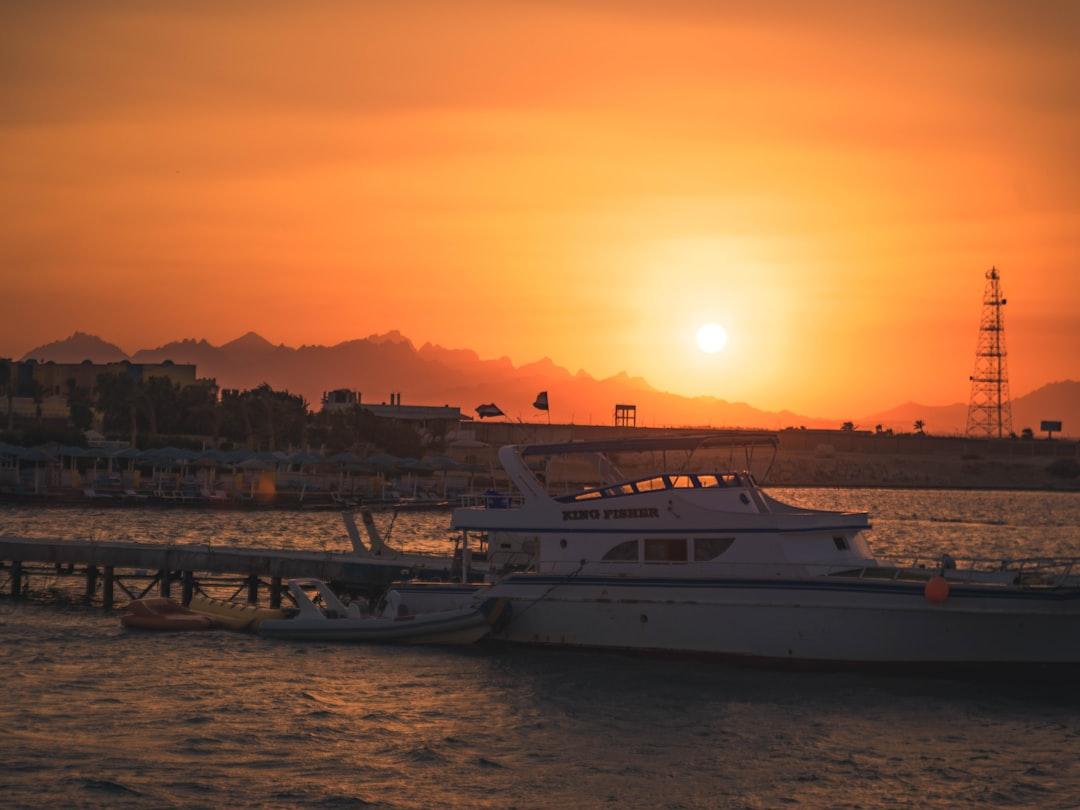 White motor yacht named King Fisher docked at Hurghada Marina pier under a vivid orange sunset over silhouetted mountains