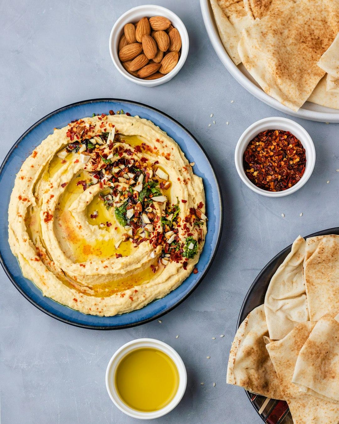 Creamy Lebanese hummus topped with olive oil, chili flakes, and chopped almonds, served with pita bread at Em Sherif Beirut