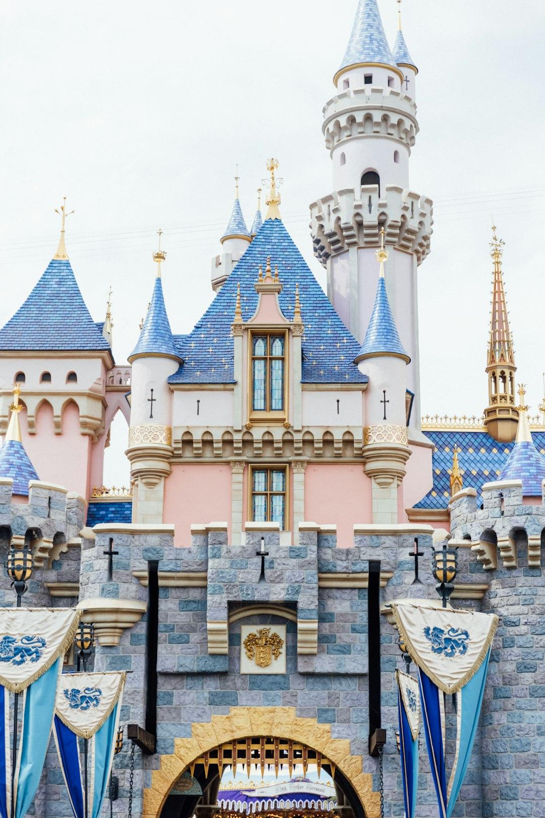 Sleeping Beauty Castle at Disneyland Anaheim with blue-tiled spires, pink walls, gold accents, and royal banners at the entrance gate