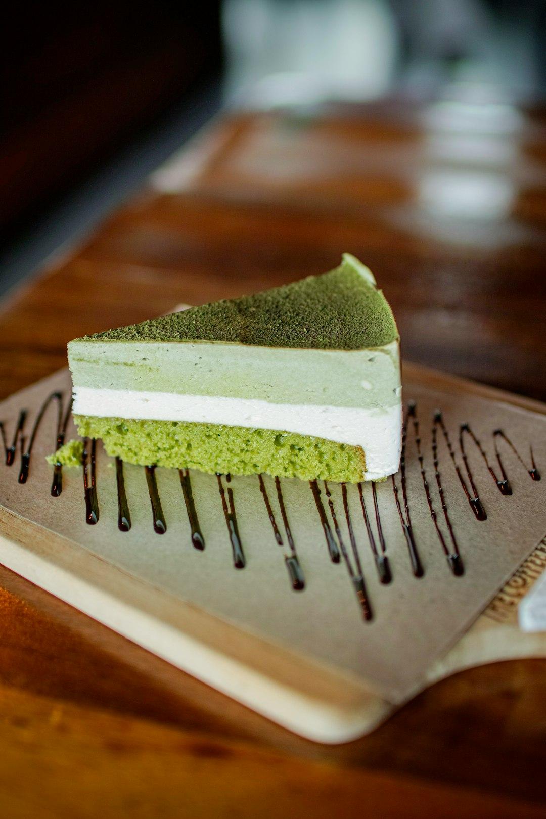 Slice of layered matcha tiramisu with green sponge base, cream filling, and matcha powder dusting on a wooden plate