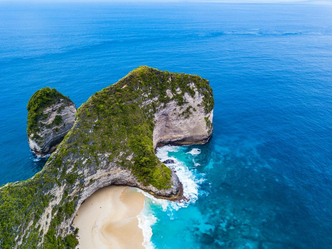 Aerial view of Kelingking Beach cliff on Nusa Penida, with lush green headland jutting into vivid blue ocean