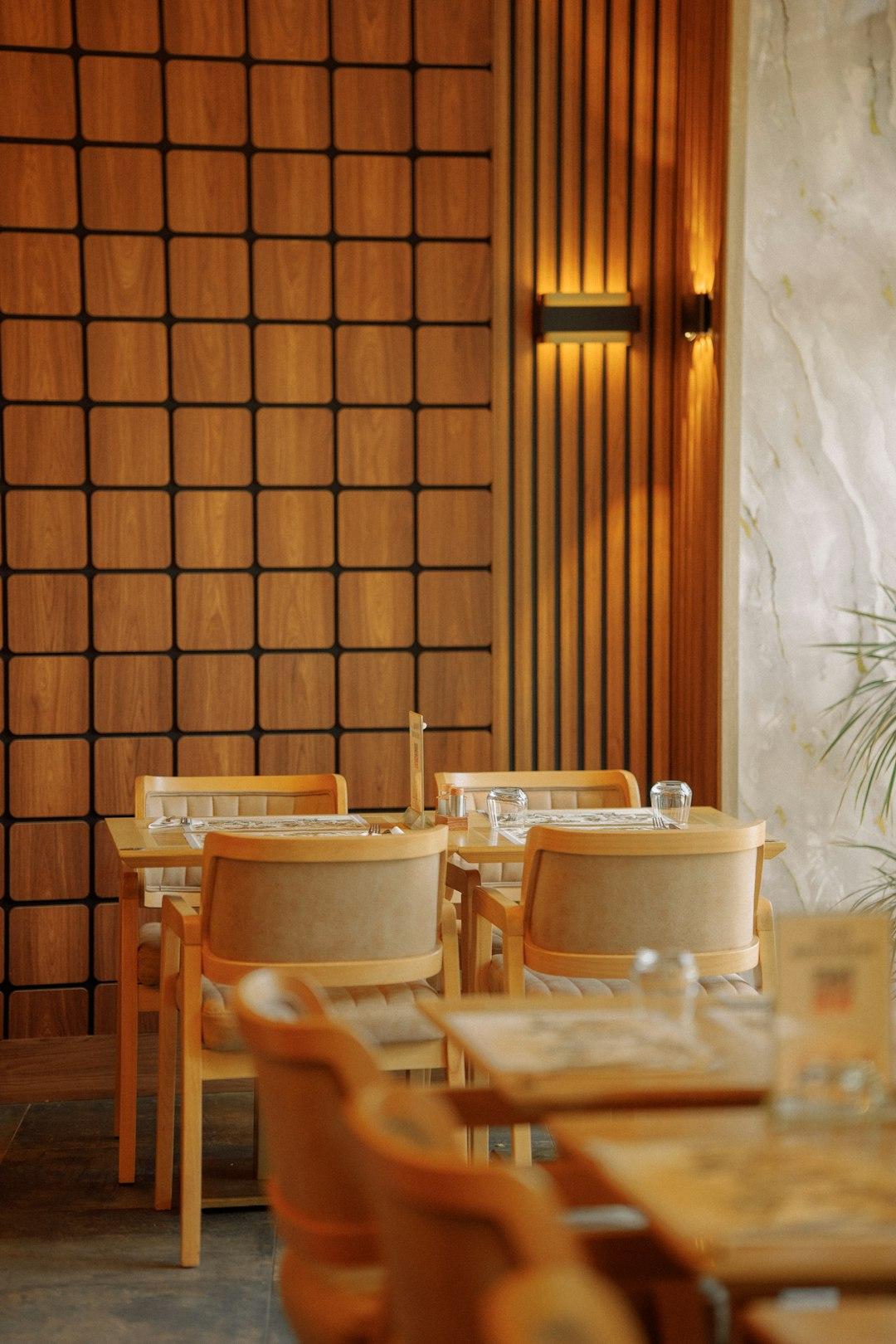 Warm wood-panelled dining room with beige upholstered chairs, set tables, and a glowing wall sconce at Sakura Japanese Restaurant, Hurghada
