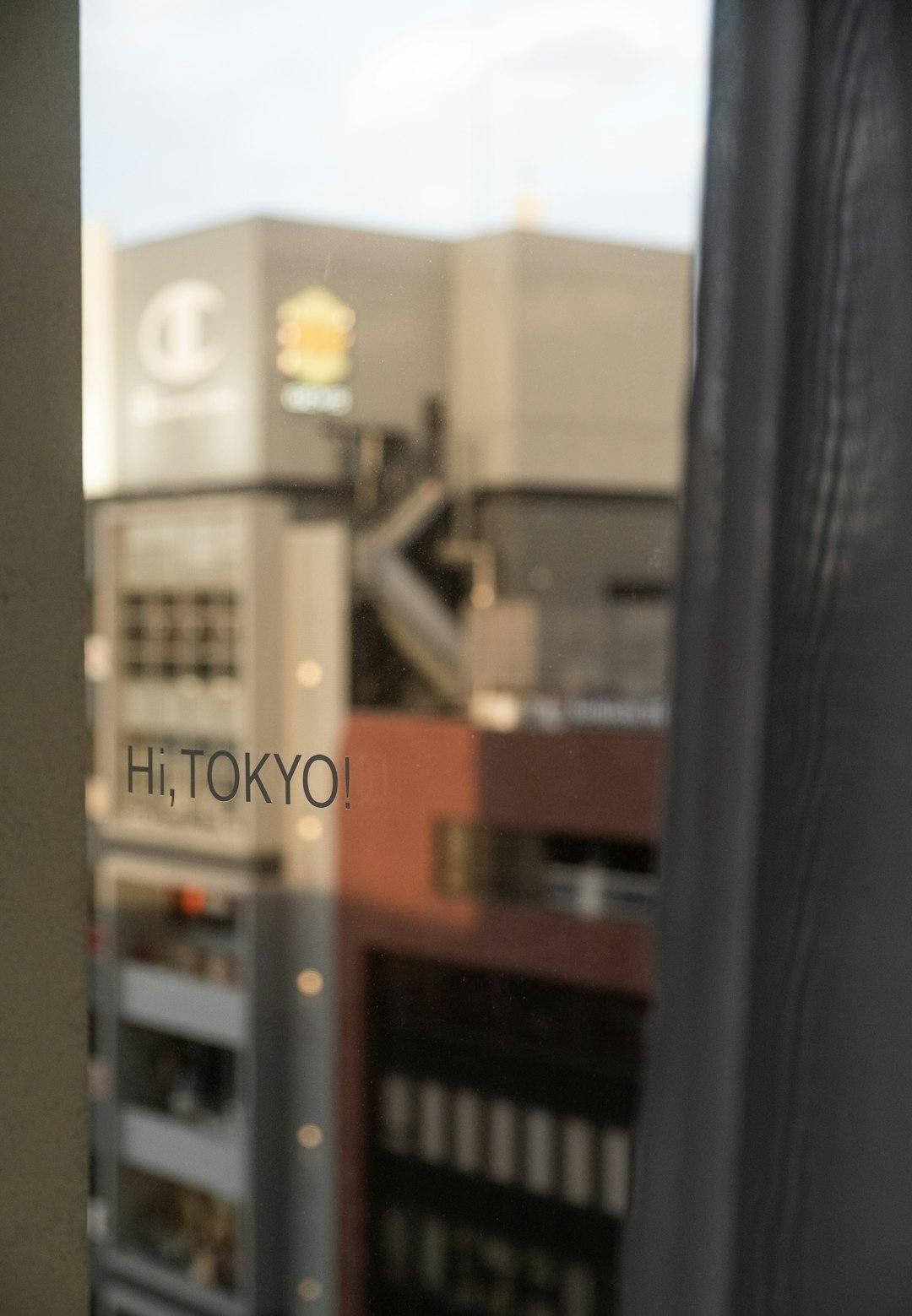 'Hi, Tokyo!' text on a glass window overlooking blurred urban buildings in central Tokyo