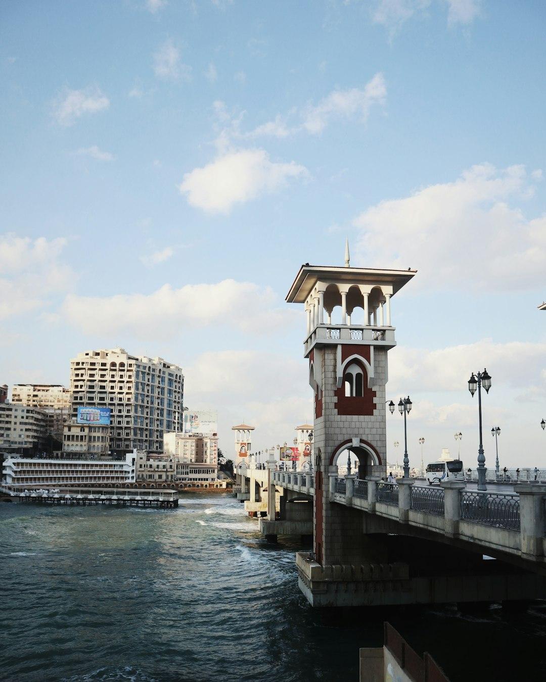Stanley Bridge in Alexandria with ornate white and red tower, iron railings, street lamps, and choppy sea below