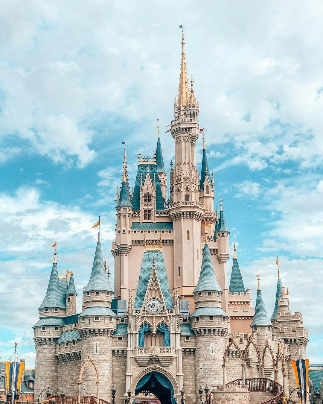 Cinderella Castle at Magic Kingdom, Walt Disney World, with teal spires and golden tips under a cloudy blue sky