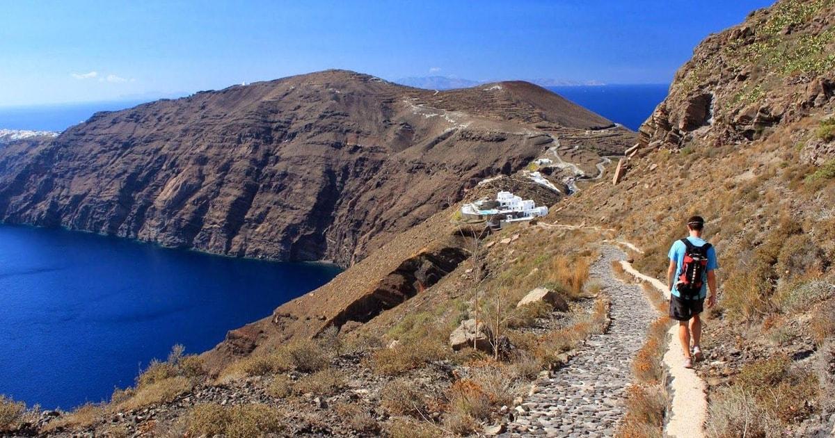 Panoramic view of Santorini's volcanic caldera with deep blue waters and rugged dark cliffs under a cloudy sky