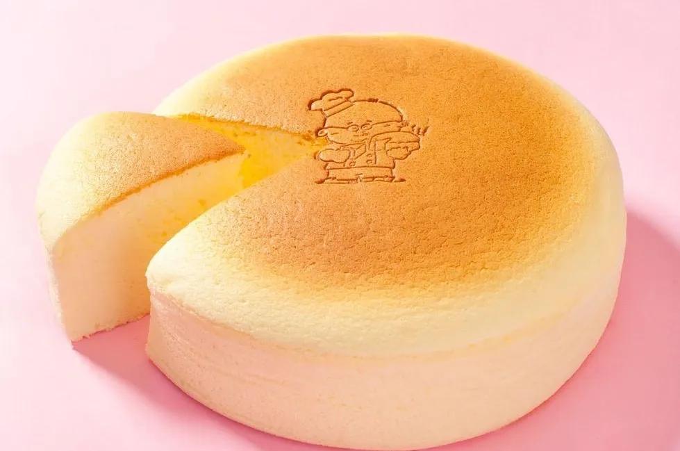 Fluffy Japanese soufflé cheesecake dusted with powdered sugar on a round wooden board, one slice cut out beside a metal cake server