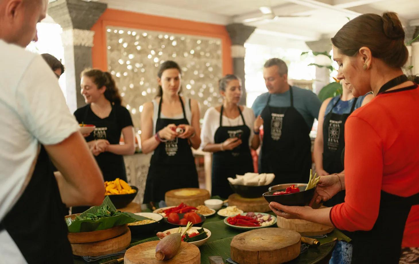 Participants grinding fresh spice paste using a traditional stone mortar at Casa Luna Cooking School in Ubud