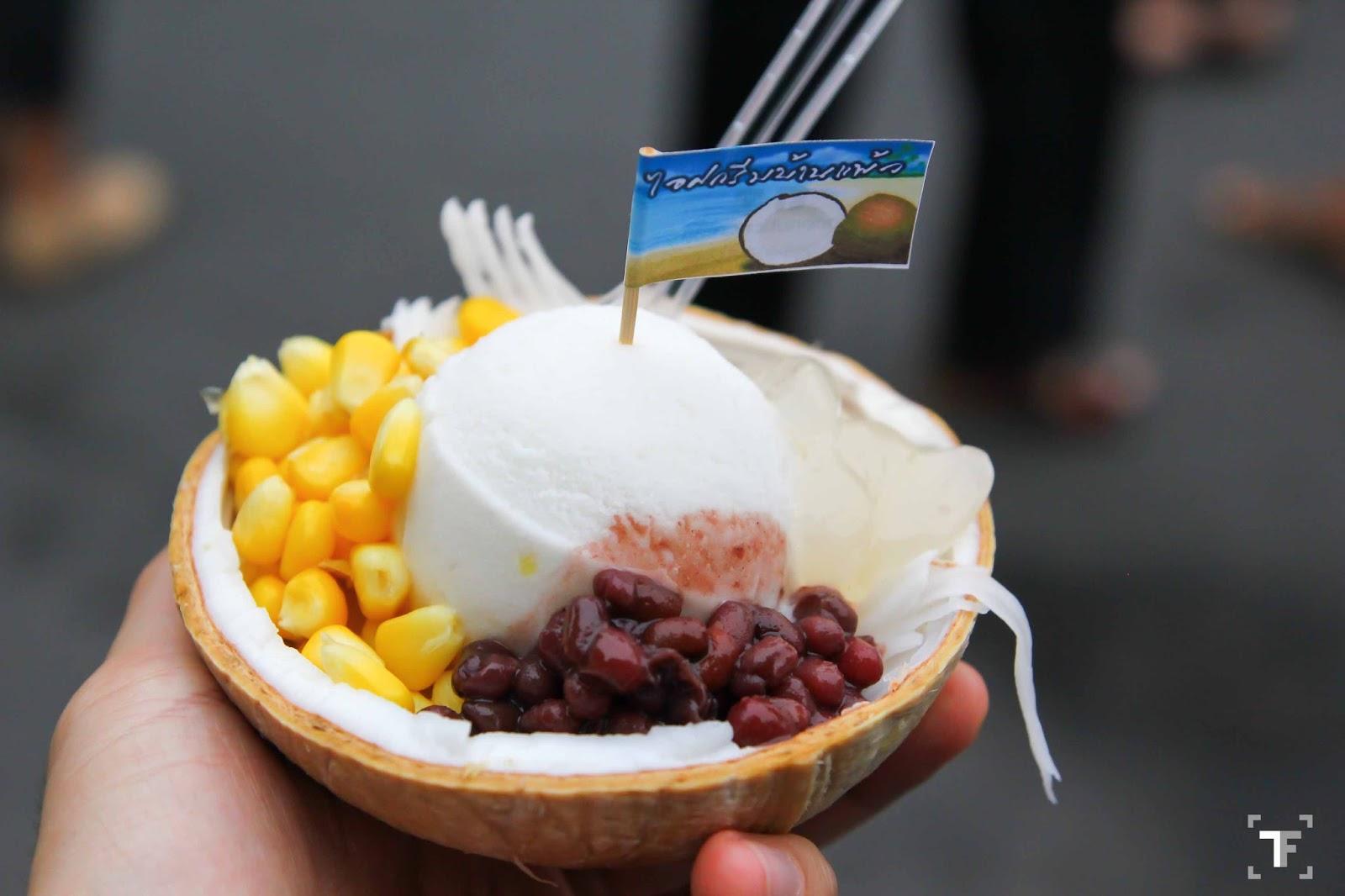Young vendor scooping coconut ice cream at a rustic Thai market stall with a handwritten sign reading 30 THB