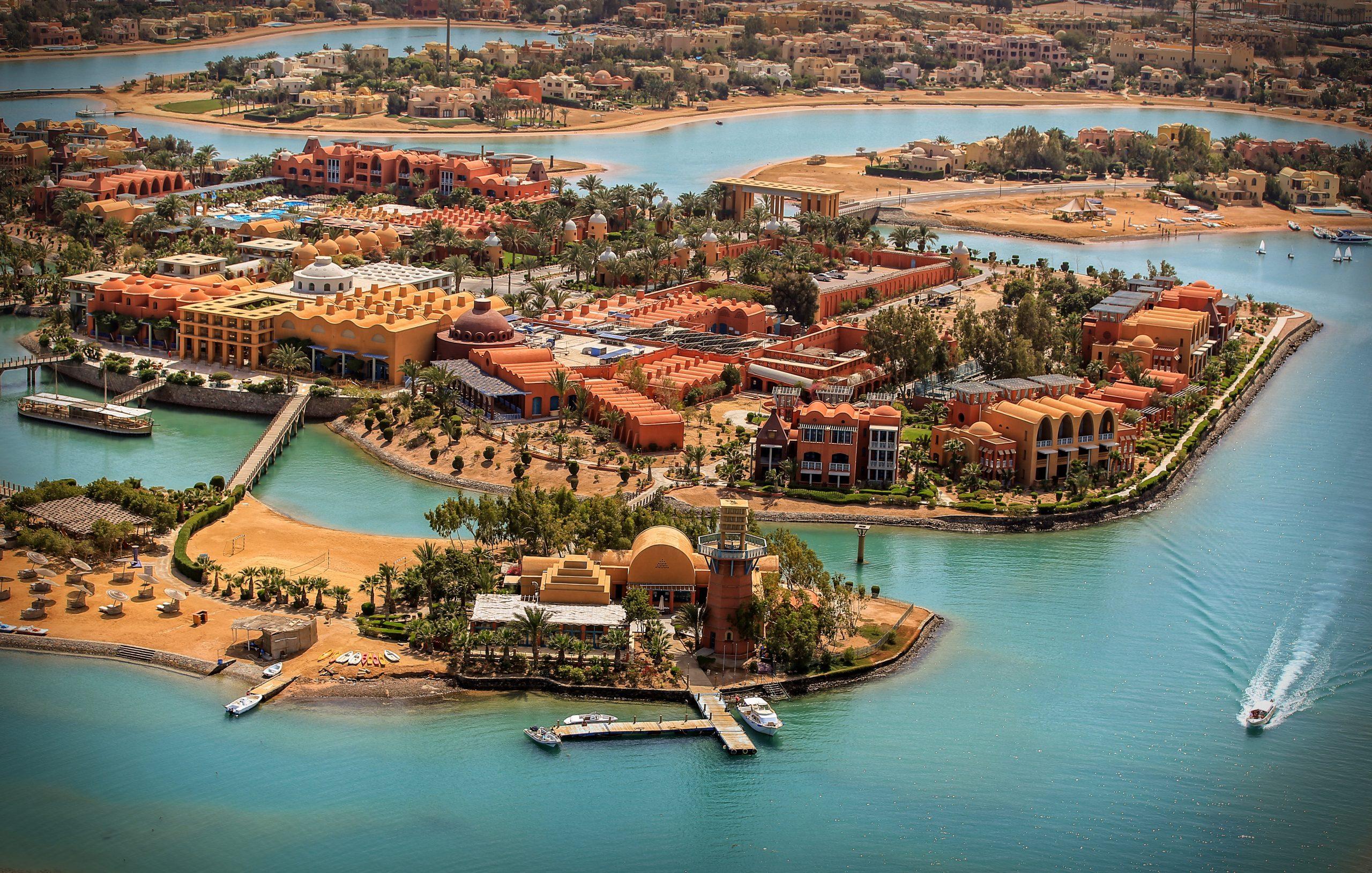 Sharm El Sheikh resort beach with straw umbrellas, palm trees, wooden pier, and mountain backdrop under clear blue sky