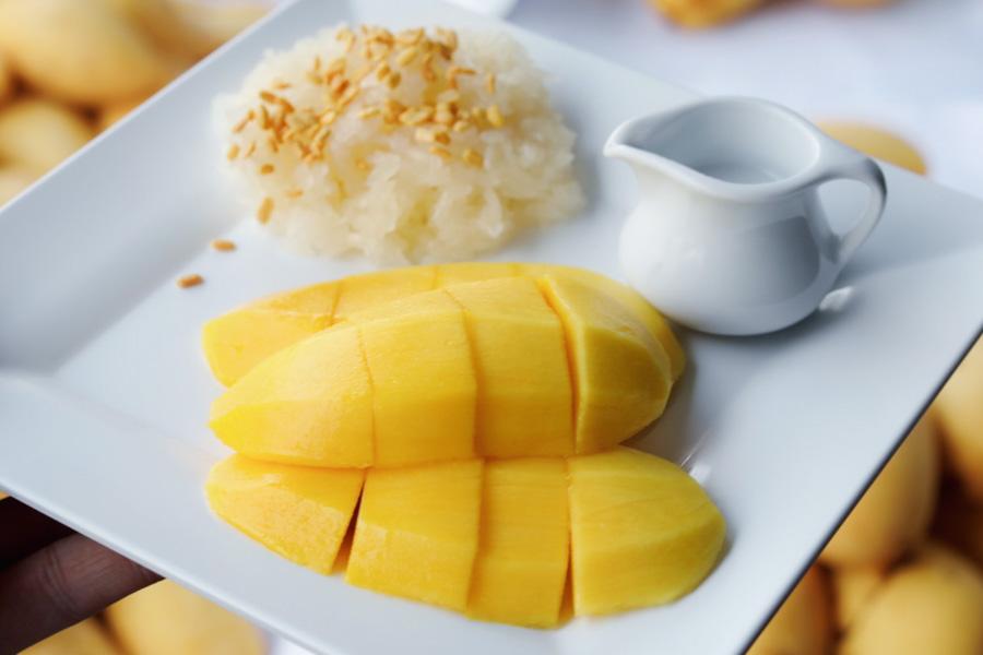 A plate of mango sticky rice with coconut cream drizzled over yellow mango slices at Kor Panich, Bangkok