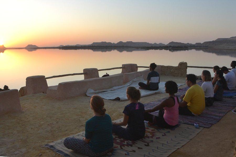 Calm blue lake surrounded by smooth golden sand dunes in Siwa Oasis, Egypt, with visitors walking along the shoreline