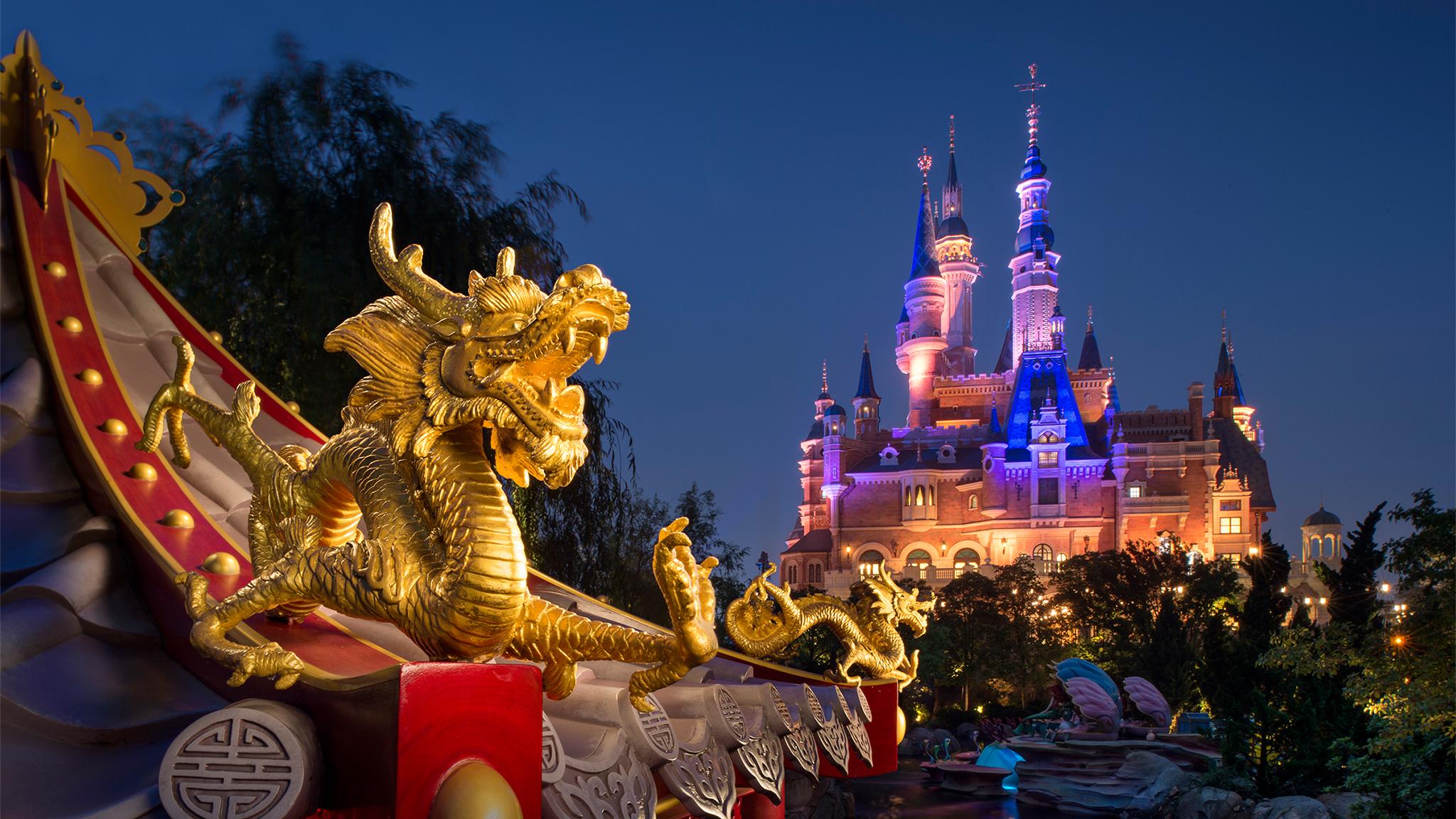Shanghai Disneyland castle illuminated in pink and purple lights at night, with ornate spires and glowing street lamps