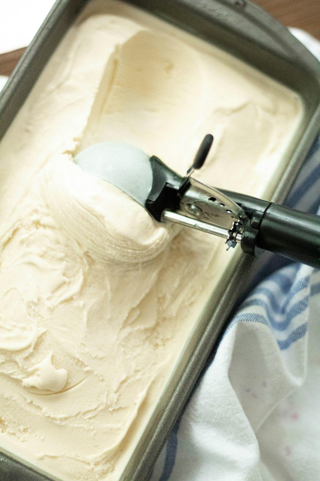 Colorful gelato scoops in a waffle cone held up against Santorini's whitewashed caldera cliffside at golden hour
