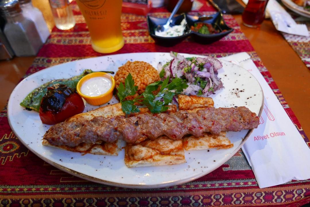 Adana kebab served on flatbread with bulgur rice, onion salad, grilled vegetables, and yogurt dip at Zübeyir Ocakbaşı
