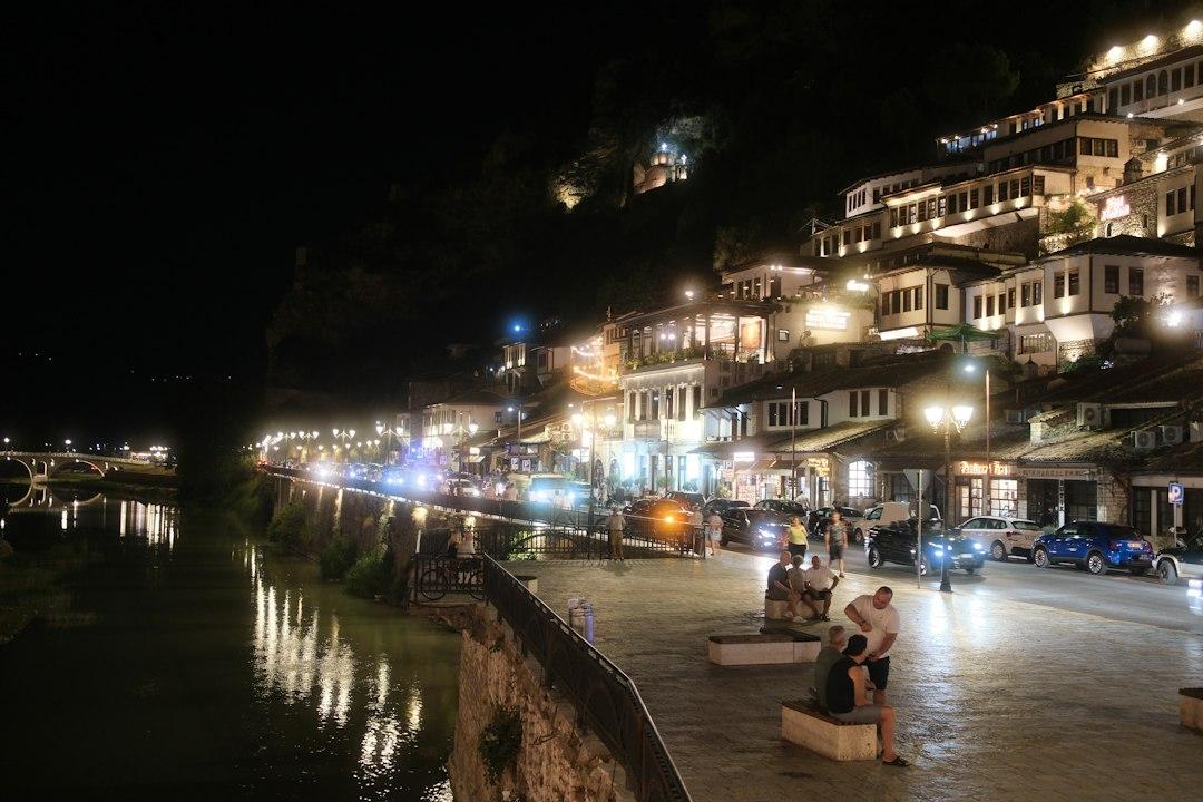 Illuminated Ottoman-style buildings stacked on a hillside along a river promenade in Berat, Albania, at night