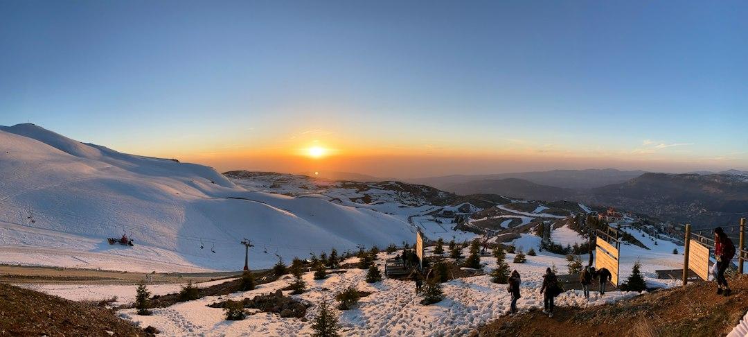 Panoramic sunset view over snow-covered slopes at Mzaar Kfardebian ski resort, Lebanon, with visitors walking along a snowy ridge