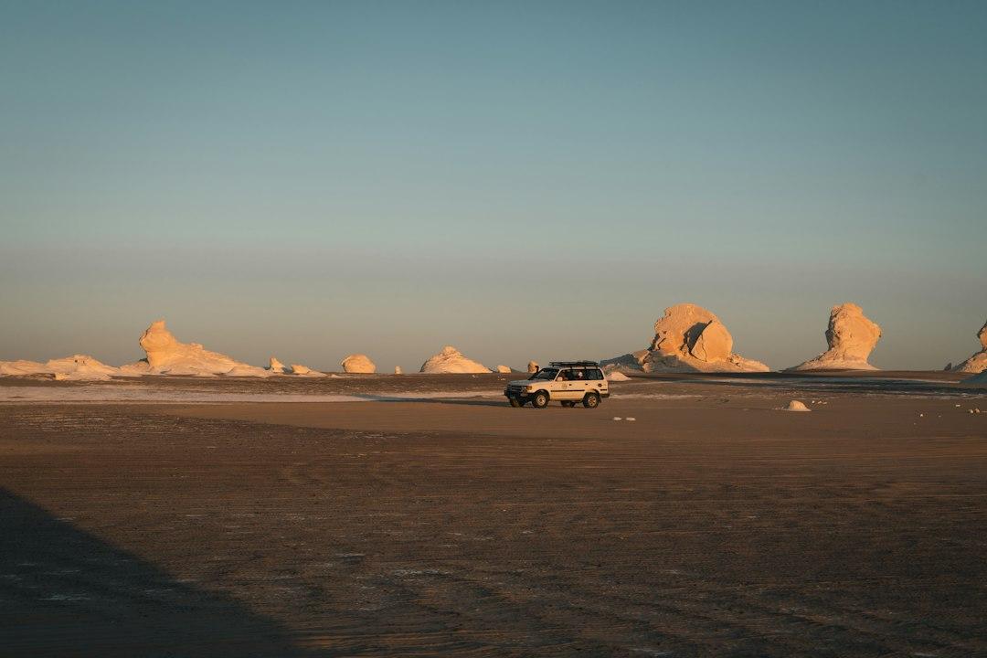 White 4WD SUV driving across Egypt's White Desert with sculpted chalk rock formations glowing golden at sunset