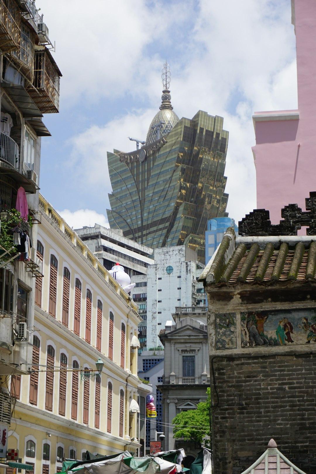 Grand Lisboa tower's golden lotus-shaped skyscraper rising above colonial Portuguese buildings and a Chinese temple rooftop in Macau